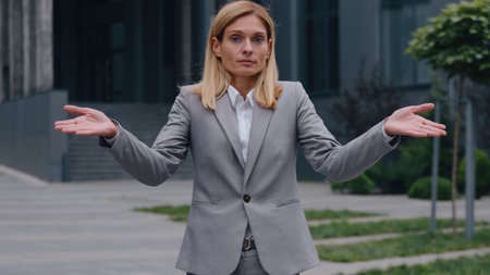 Confused Caucasian middle-aged business woman shrug shoulders hands to side unsure adult businesswoman female puzzled entrepreneur executive lady worker in city in downtown spread arms feeling doubtの写真素材