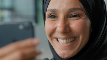 Portrait happy arabian business woman in hijab smiling looking in phone laughing smile Muslim businesswoman female girl with smartphone app carefree emotional joyful look in mobile smartphone emailの写真素材