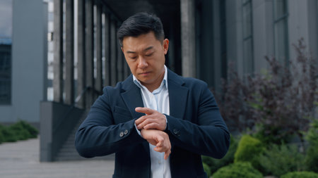 Chinese middle-aged business man feeling anxiety checking time on wristwatch Asian Korean businessman late in city waiting hurry meeting male wait Japanese specialist sad with appointment impatientの写真素材