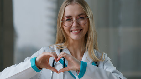 Caucasian happy smiling woman doctor showing heart shape cardiologist nurse female girl show cardio gesture looking at camera practitioner therapist working in clinic hospital medicine health careの写真素材