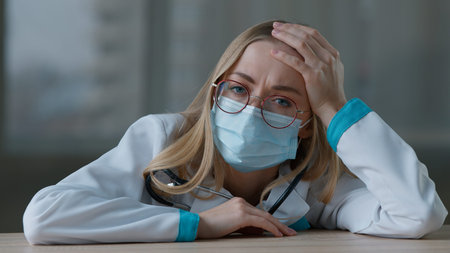 Napping ill tired Caucasian woman doctor in uniform face medical mask overload overtime working in...