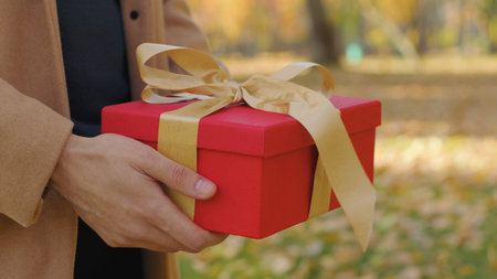 Close unrecognizable couple with gift box in city unknown man boyfriend congratulate woman girlfriend giving present with gold ribbon anniversary birthday surprise in autumn park love affectionateの写真素材