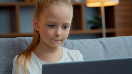 Caucasian child girl typing laptop at home focused little kid daughter pupil schoolgirl user studying with computer distant education playing at cyberspace communicate in internet chatの写真素材