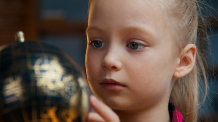 Close up little Caucasian child kid girl daughter rotating gold globe studying at evening home baby exploring world search countries dreaming traveling study geography planet cartography navigationの写真素材