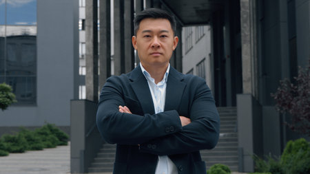 Motivated serious 40s Chinese ethnic business man crossing hands looking at camera Japanese middle-aged businessman adult Asian Korean male entrepreneur formal manager crossed arms power pose in cityの写真素材