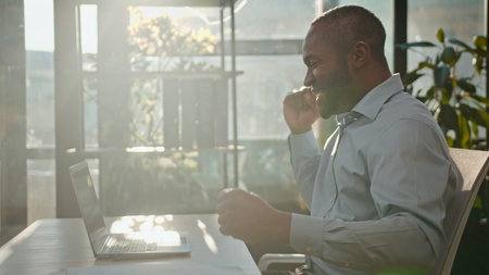 Happy African American business man with laptop dancing at sunlight sunny office active moving joyful adult businessman male porofessional dance listening music celebrating victory having fun rejoiceの写真素材