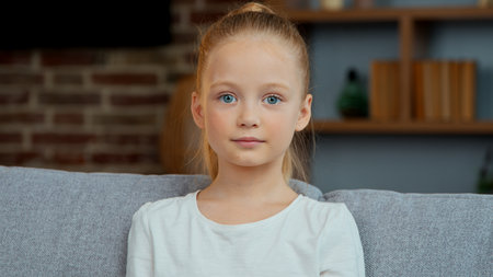 Portrait happy Caucasian cute girl kid daughter child smiling looking at camera carefree positive cheerful posing at home living room satisfied adorable baby schoolgirl joyful smile in cozy apartmentの写真素材