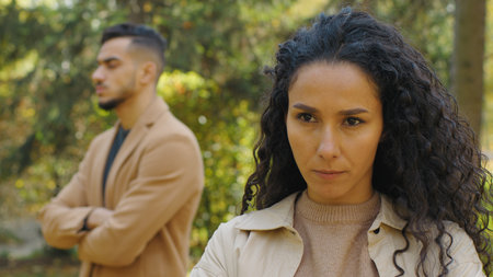 Woman with frown standing in autumn park with man in background after quarrel misunderstandingの写真素材