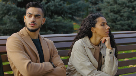 Couple separated sitting on bench in autumn park family problem conflict sad serious man with woman spouses in city silent trouble after quarrel misunderstanding breakup relationshipの写真素材