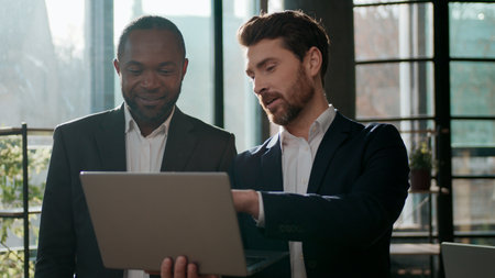 Diverse business team men colleagues cooperation with laptop online internet using web cyberspace work in office talking partners multiracial businessmen discuss corporate success project technologyの写真素材