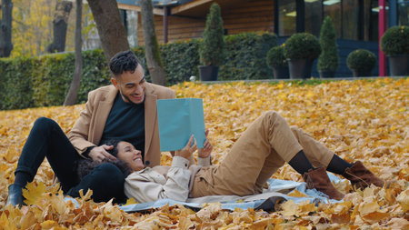 Couple date outdoors in romantic autumn park with reading book man listening beloved woman read loud story literature family married guy girl enjoying weekend in nature fall seasonの写真素材