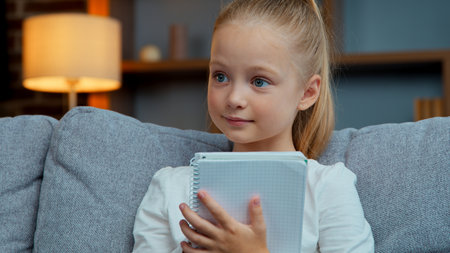 Caucasian smiling happy little child girl writing in textbook at home distant education learning studying kid daughter schoolgirl enjoying elementary primary study in living room school write taskの写真素材