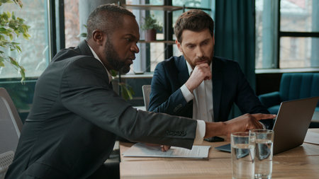 Two diverse men multiracial business team solving work online project problem discussing internet computer task worried with trouble laptop in office Caucasian African American businessmen partnershipの写真素材