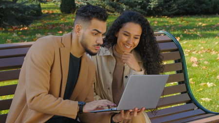 Pensive hispanic couple looking in laptop talking decide solution in autumn park in city on bench family thinking discussing computer shopping purchase buying talk together smileの写真素材