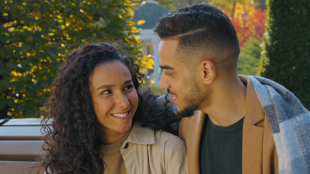 Cute couple covered with plaid blanket date in autumn park on bench in city smiling cuddling talking love dating affectionate woman enjoying cuddle with beloved man outdoorsの写真素材
