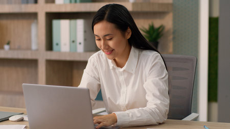 Positive Asian Japanese girl office worker employer HR manager business woman joyful Korean female businesswoman talking online video call computer laptop meeting interview recruiting indoors companyの写真素材