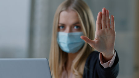Caucasian business woman in medical face mask with laptop showing stop gesture no palm sign businesswoman girl female employer hand not never forbid deny reject keep distance pandemic covid19 rulesの写真素材
