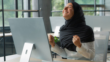 Happy Muslim business woman win with computer Arabian businesswoman female girl worker employer winning victory success with pc in office Islamic lady achieve good result internet company web growthの写真素材