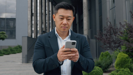 Asian happy business man walking in city chatting phone Korean businessman walk going outside office texting mobile app smiling Chinese middle-aged Japanese male worker go browsing web gadget onlineの写真素材