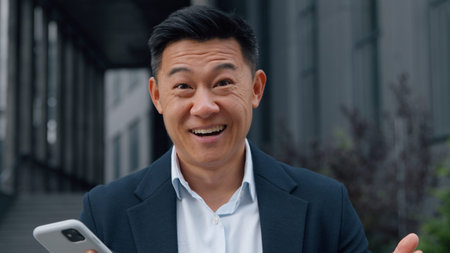 Happy excited businessman business man amazed with phone mobile money win looking at camera with open mouth big eyes Asian male with smartphone in cityの写真素材