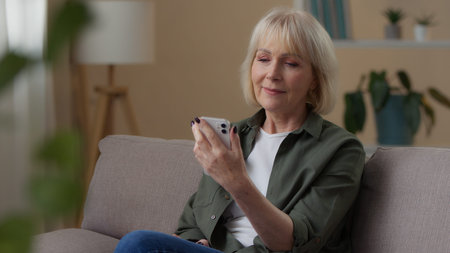 Old Caucasian woman looking in phone thinking at home relaxed 60s senior female retired lady using...