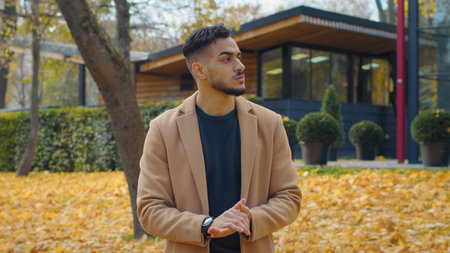 Worried Hispanic man guy in autumn park look around waiting for meeting looking searching disappointed nervous wait sad male standing outdoors in fall season city lateness problem cancel appointmentの写真素材