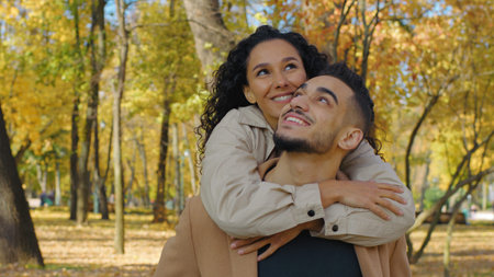 Hispanic couple in love piggyback in autumn park hugging cuddling affectionate relationship girl...