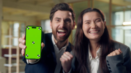 Excited two business woman man celebrating win showing mobile phone green screen chroma key mock up Caucasian Korean businesspeople cheering winner victory money smartphone excitement triumph officeの写真素材