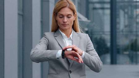Serious Caucasian middle-aged business woman checking time with wristwatch in city looking around waiting meeting adult businesswoman female worker executive entrepreneur check clock lateness problemの写真素材