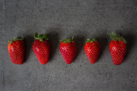 Fresh strawberries in a row on dark grey table. Flat lay photo.