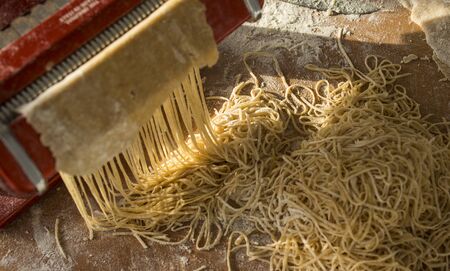 Red pasta maker and dry spaghetti on wooden table. Food photo.の写真素材