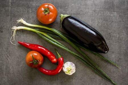 Green onion, red pepper, tomato, eggplant and garlic on dark grey table. Fresh vegetables and spices top view photo.の写真素材
