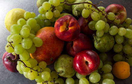 Beautiful fresh fruits on dark grey table: green grapes, nectarines, apricot. Summer fruits top view.の写真素材