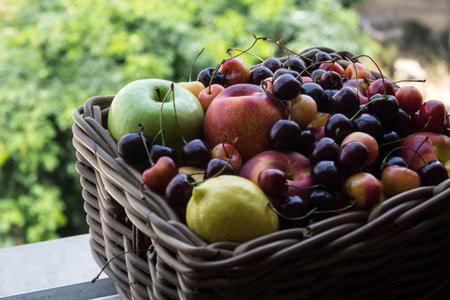 Basket full of fruits on green leaves background. Juicy summer fruits close up: cherry. apple,...