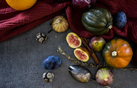 Fresh autumn vegetables and fruits on dark grey table. Top view photo of gem squash, plums, juicy figs, rosemary and silver spoon. Red textured cotton towel on background.の写真素材