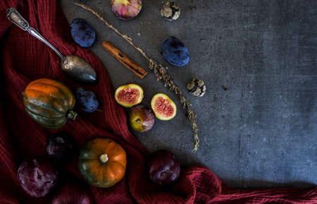 Fresh autumn vegetables and fruits on dark grey table. Top view photo of gem squash, plums, juicy figs, rosemary and silver spoon. Red textured cotton towel on background.の写真素材