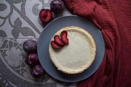 Homemade cheesecake decorated with red plums. Top view photo on grey background with copy space.の写真素材