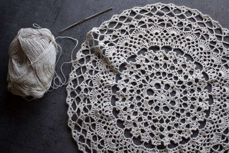 Ecofriendly decor element. Top view photo of crochet table cloth, ball of linen yarn and crochet hook. Dark grey background with copy space. Hobbies and crafts concept.の写真素材