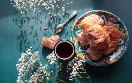 Sweet breakfast close up photo. Freshly baked croissants on a blue plate. French cuisine. Still life with flowers and sweet pastries.の写真素材