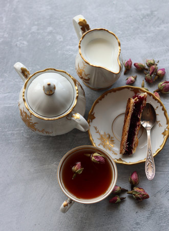 Still life with cup of tea,  jug of milk, cherry pie, small rose flowers. White vintage tableware on a table.  Sweet breakfast close up photo.の写真素材