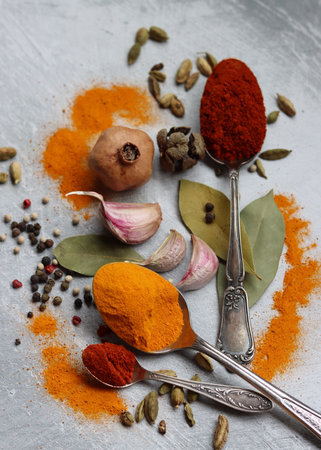 Still life with silver spoons, turmeric , paprika powder, bay leaf and pepper. Vibrant colors of Indian spices. Aromatic spices and herbs on a table. Food seasonings texture close up.の写真素材