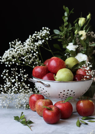 Fresh red apples in a colander on a dark background with flowersの写真素材