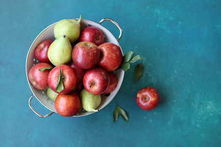 Red apples and pears in a colander on turquoise backgroundの写真素材
