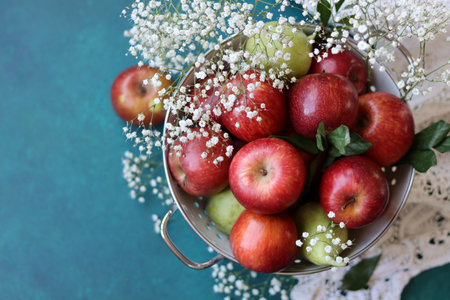Bowl of fresh red apples and flowers on turquoise backgroundの写真素材