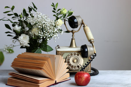 Retro phone, rusty alarm clock, red apple gypsophila flowers on a desk. White background with copy space. Retro objects still life photo.の写真素材