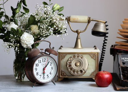 Vintage telephone, alarm clock and flowers in a vase.