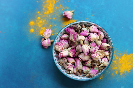 Dried rose buds in bowl with turmeric powder on blue backgroundの写真素材