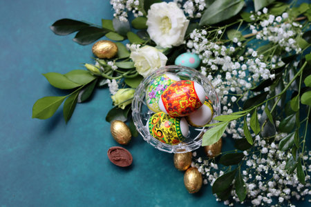 Easter eggs and flowers on turquoise background, top view