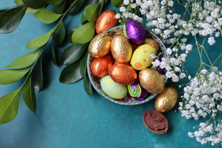 Easter composition with chocolate eggs, flowers and green leaves on color backgroundの写真素材