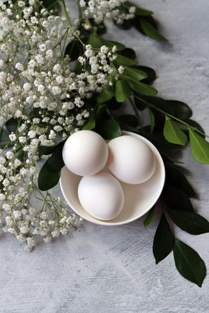 Easter eggs in a bowl and white flowers on a gray backgroundの写真素材